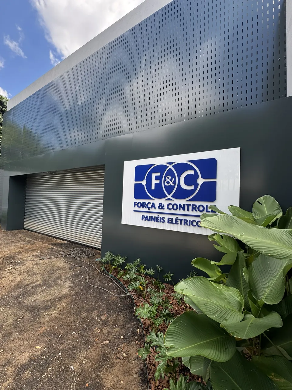 Placa branca com logotipo azul fixada em fachada escura com parede perfurada