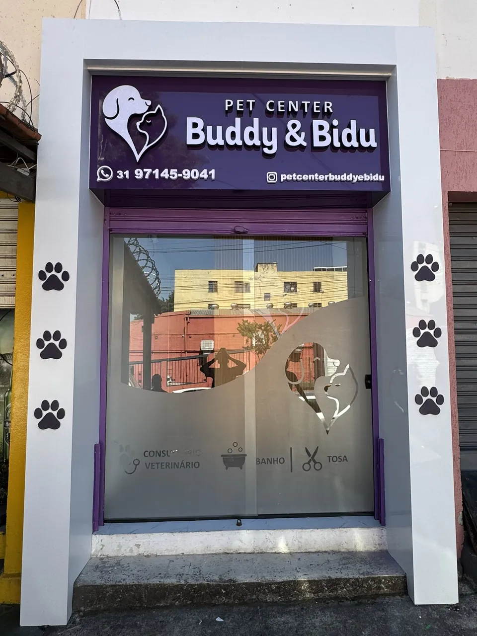 Fachada de pet center com moldura branca, painel roxo com logotipo e porta de vidro adesivada