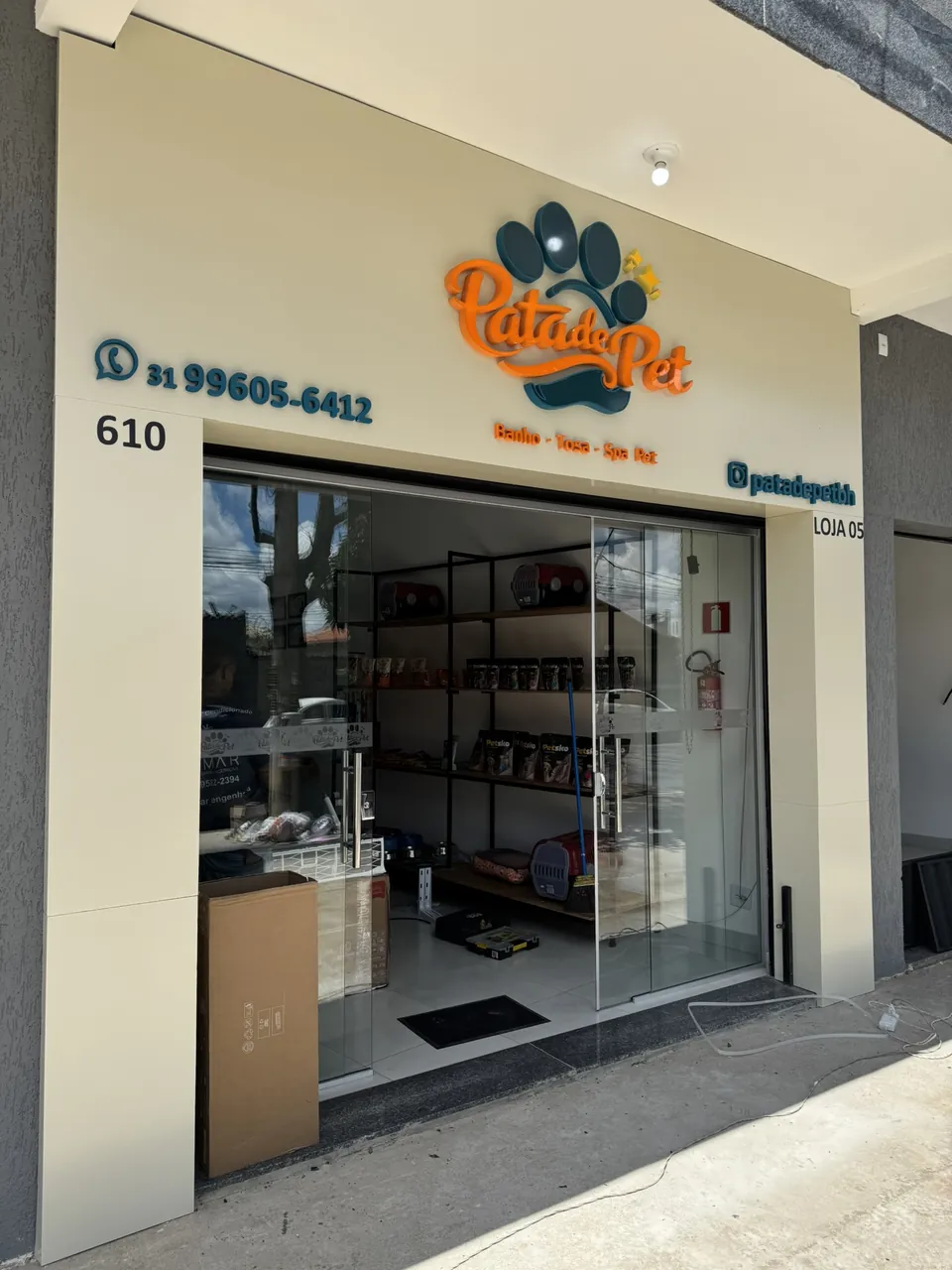 Fachada de pet shop com logotipo laranja e azul em relevo, contatos aplicados e porta de vidro