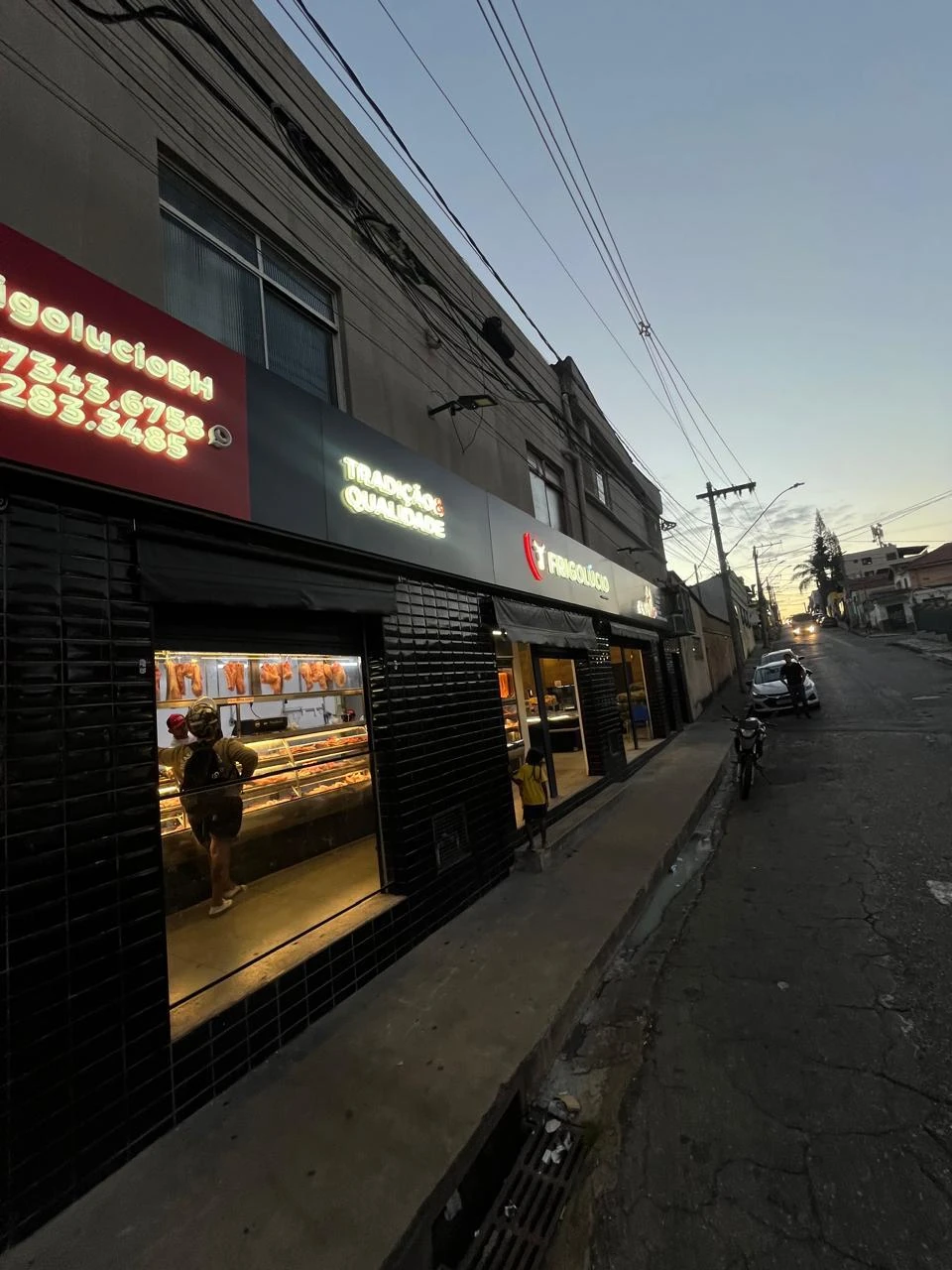 Fachada de açougue iluminada à noite, com letreiro em neon verde