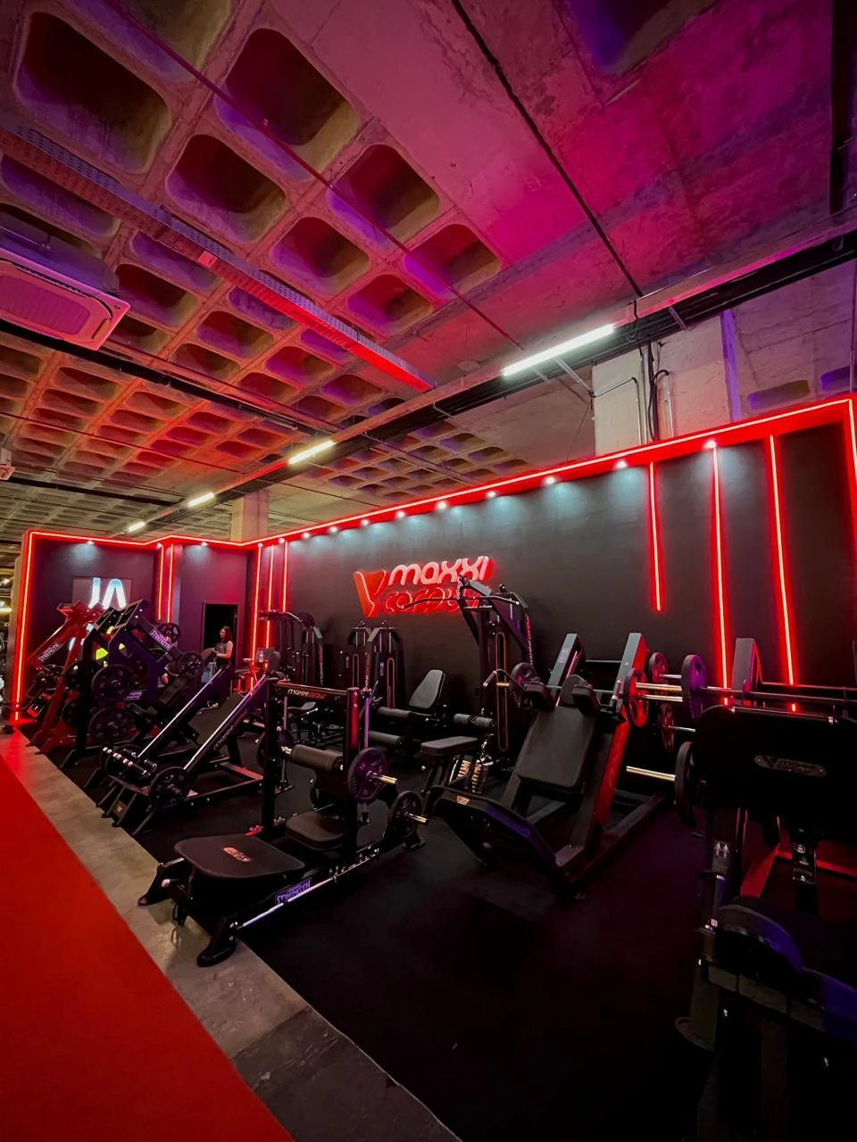Estande com aparelhos de musculação sob iluminação em neon vermelho e letreiro iluminado, em pavilhão de feira
